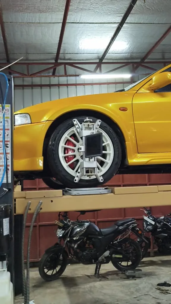 Yellow car on the alignment lift with a sensor clamp on the front wheel.