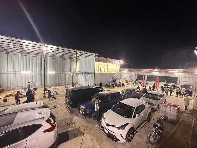The M & M Car Clinic yard at night, cars parked under the lit service sheds.